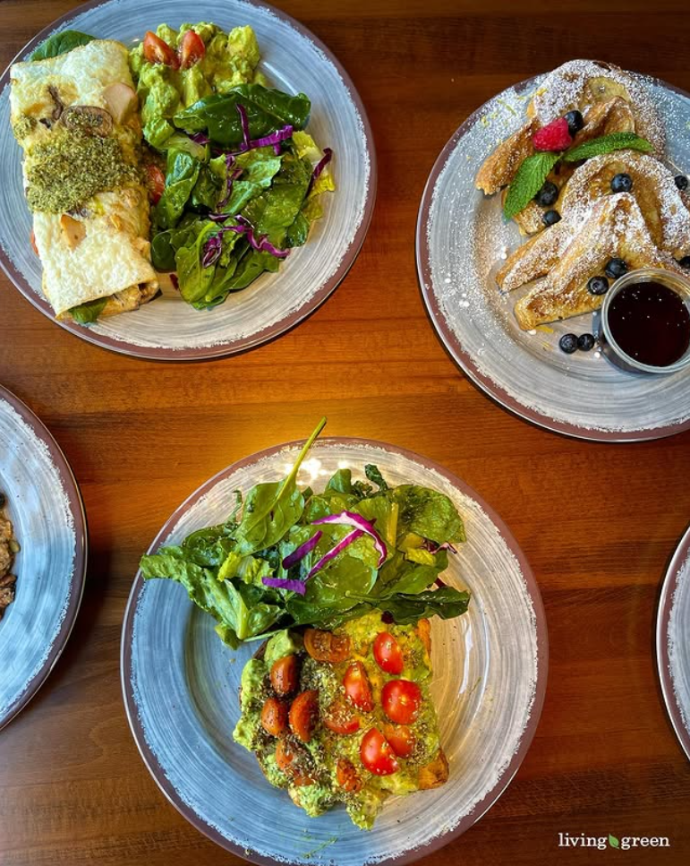 Overhead view of a Living Green Cafe brunch spread: breakfast wrap, French toast, and avocado toast with salad