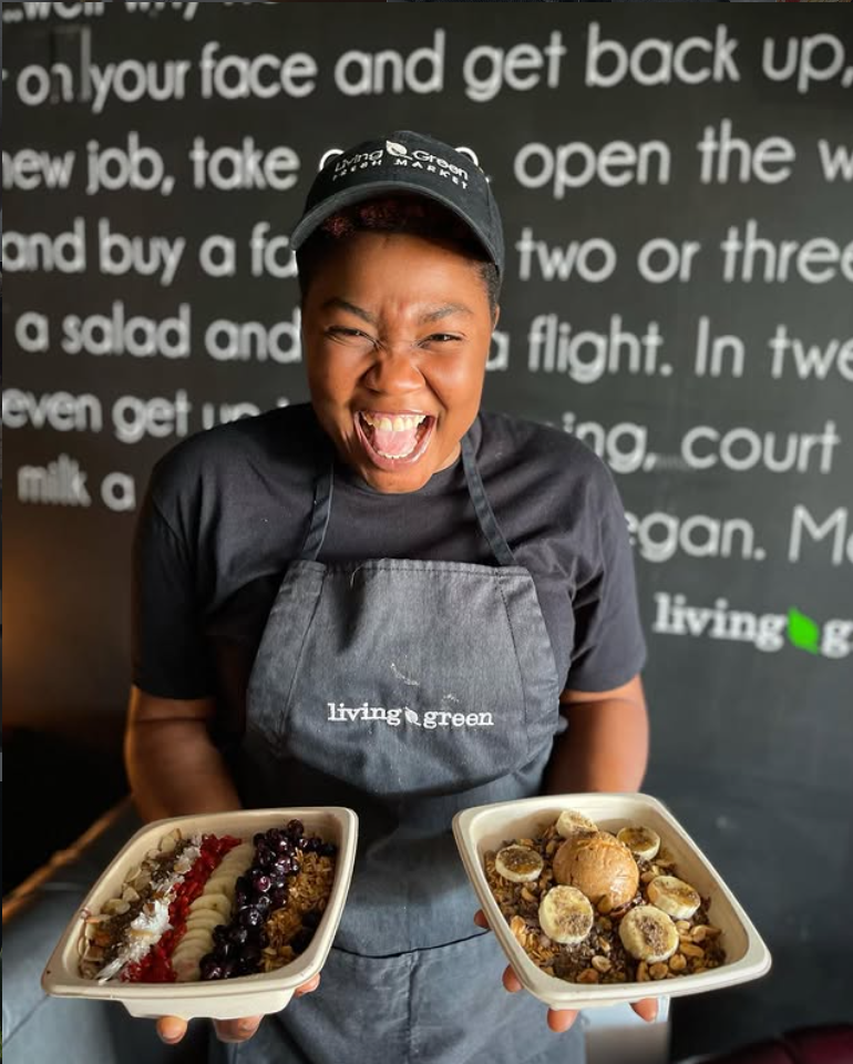 Smiling Living Green Cafe staff member holding two acai bowls topped with banana, blueberries, and granola
