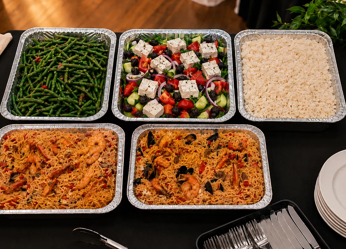 Catering trays over a table, beans, rice, shrimp and Greek Salad